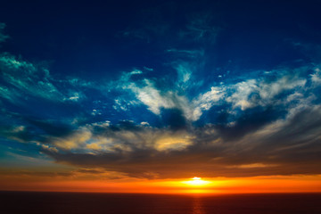Fototapeta na wymiar sun setting over a sea horizon behind dramatic cloudscape