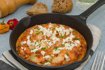 National greek dish saganaki with shrimps. Shrimp saganaki with tomato and feta cheese in a pan. Homemade shrimp and tomato sauce with feta in pan on napkin top. 