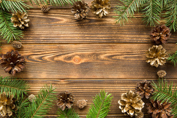 Fototapeta na wymiar Pine golden cones and fir tree branches branches on brown wooden background. Free space for text. Christmas mood background.