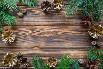 Pine golden cones and fir tree branches branches on brown wooden background. Free space for text. Christmas mood background.