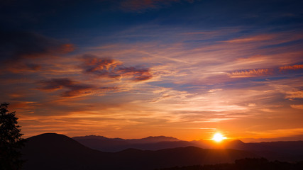sun setting behind silhouetted mountains in a blue sky with travelling clouds