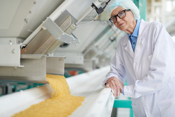 Waist up portrait of  smiling senior woman standing by machines inspecting macaroni production at food factory , copy space