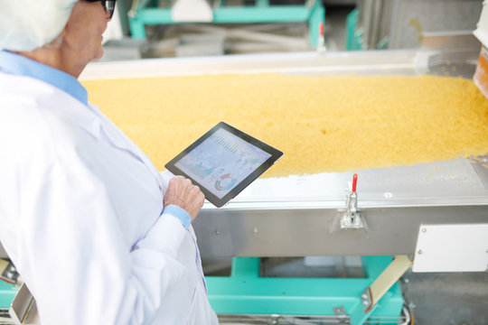 High angle portrait of senior factory worker using digital tablet standing by machine units at modern food production plant, copy space