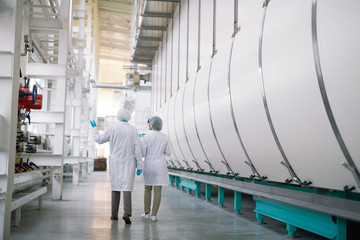 Back view full length portrait of two factory workers wearing white coats crossing production...