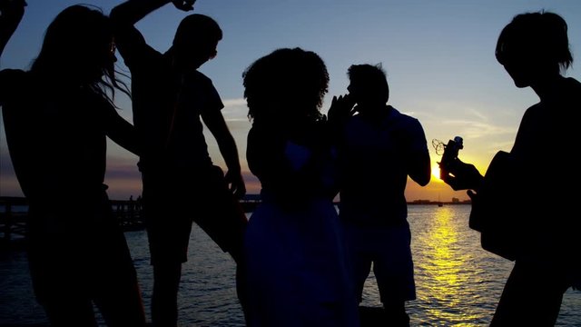 Silhouette of people dancing and playing the guitar on the beach party at sunset