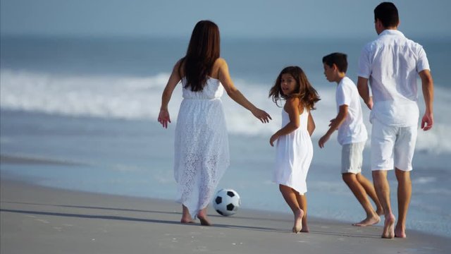 Hispanic family playing together on beach holiday with soccer ball