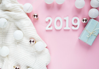 Christmas concept flat lay. Warm, cozy white winter clothing, 2019 number and Christmas decorations frame on pink background