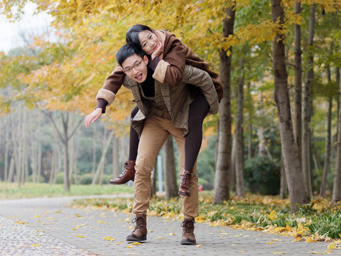 Portrait of smiling young girlfriend piggyback boyfriend during romantic walk in autumn park alley, excited couple looking at camera have fun outdoors, playing foolish, man carry lover on his back.