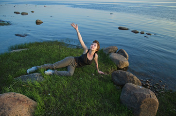 happy young woman resting on the grassy beach and smiling stretches her hand to the sky