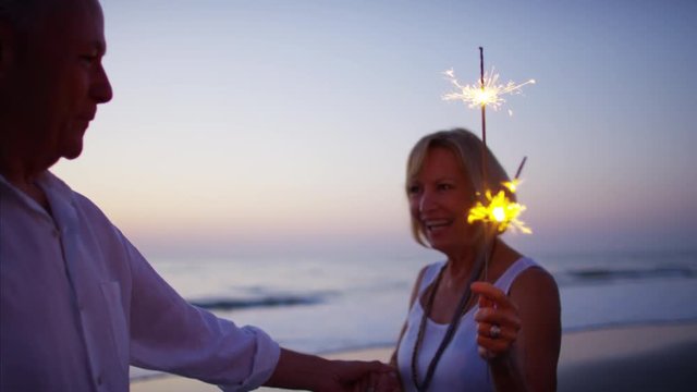 Happy Caucasian seniors having fun with sparklers on the beach at sunset