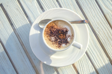 cup of cappuccino with latte art on wooden white table. top view