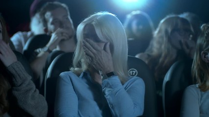 Struggling woman in a movie theatre audience watching a horror film.