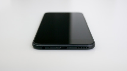 Modern black smartphone on white desk showing USB type C / USB-C port and headphone jack. Shallow depth of field.