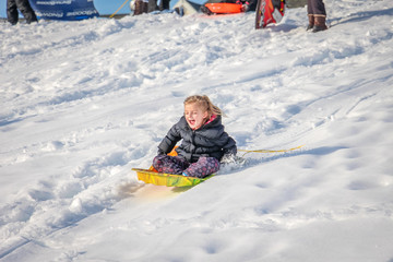 Fototapeta na wymiar Cute Little Girl Smiling as She Sleds Down Hillside Covered With Snow