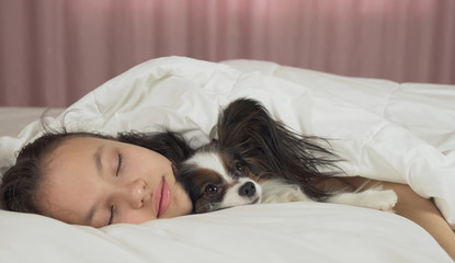Beautiful teen girl sleeping sweetly in bed with Papillon dog