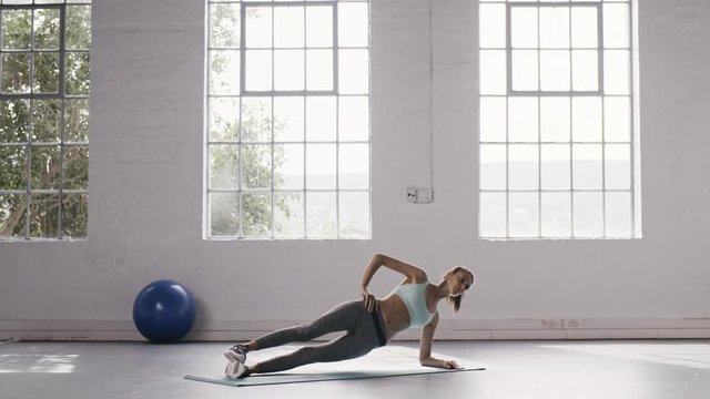 Fitness woman doing side planks workout at gym. Female doing core exercises at fitness studio.