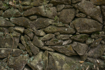 Very old dry stone wall with moss, lichen and leaves. Brown and grey rocks with worn texture.