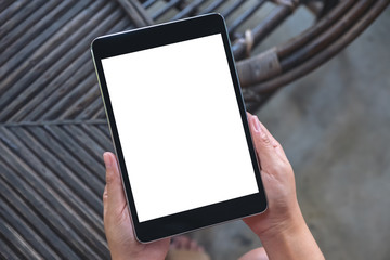 Top view mockup image of hands holding and using black tablet pc with blank white desktop screen while sitting in outdoor