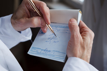 A doctor writing a prescription on a blue prescription pad. - obrazy, fototapety, plakaty
