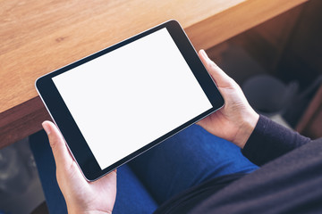 Top view mockup image of a woman holding black tablet pc with blank white screen while sitting on a chair