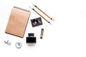 Chinese or japanese calligraphy pattern. Hieroglyph in craft paper notebook and writing accessories on white background top view copy space