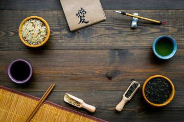 Chinese traditional symbols concept. Tea, rice, hieroglyph symbol, bambootabe mat, chopsticks, soy sause on dark wooden background top view frame copy space