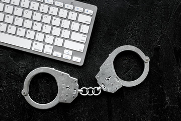 Cyberfraud concept. Handcuff near keyboard on black background top view space for text closeup