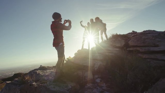 Man taking picture of his friends having fun during hike. Group of hikers enjoying themselves and taking photographs with mobile phone.