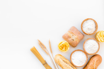 Products made of wheat flour. White flour in bowl, wheat ears, fresh bread and raw pasta on white background top view space for text