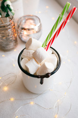 Fototapeta na wymiar White marshmallows in a cup, christmas candy canes and toy sledge on a white table. Christmas xmas new year theme