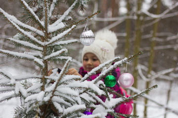 happy girl decorates the tree in the forest with balls and tinsel
