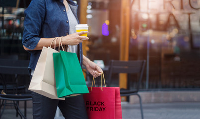 Black friday. Woman with coffee cup in hand and holding shopping bag while walking on the shopping mall background.