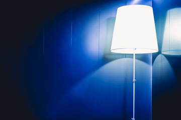 A lamp with blue rounded corners lit up on a wall surrounded by a deep dark shadow,Vintage effect style picture.