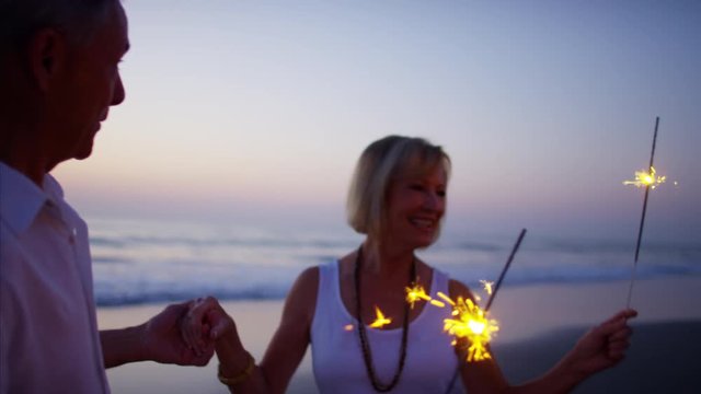 Senior Caucasian couple dancing with sparklers on the beach at sunset
