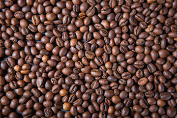Texture and background of roasted coffee beans scattered on the table with side light from a pulsed source