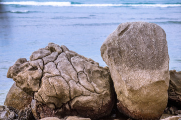 The background of a large rock, located on the sea, is a wave of coastal erosion.