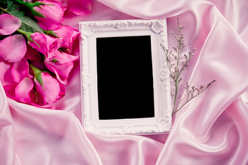 Empty photo frame with  bouquet sweet pink roses  petal on  soft pink silk fabric , romance and love card concept