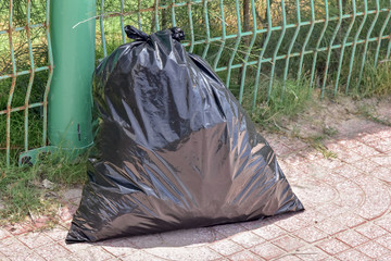 Black garbage bag next to green fence