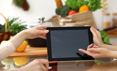 Close-up of human hands using tablet or touch pad. Two women in kitchen. Cooking, friendship or online shopping concepts