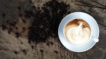 Cappuccino or latte art coffee. Free hand pouring some foam of milk on top. A white ceramic cup on the wood table with some coffee beans. The best food and drink in the world. Fresh energy everyday.