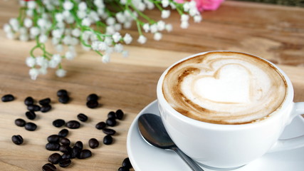 Cappuccino or latte art coffee. Free hand pouring some hearts of milk on top. A white ceramic cup on the wood table with some coffee beans. The best food and drink in the world. Fresh energy everyday.