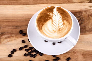Hot cappuccino or latte art coffee. A cup of coffee on the wooden table with roasted beans. Morning breakfast with coffee. Flowers shape created by pouring steamed milk.
