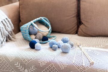 Knitting in cozy home interior. Woolen balls dropped from blue wicker basket with yarn on sofa. Winter or Christmas mood, atmosphere. Concept of woman's hobby, leisure.