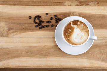 Hot cappuccino or latte art coffee. A cup of coffee on the wooden table with roasted beans. Morning breakfast with coffee. Hearts shape created by pouring steamed milk.