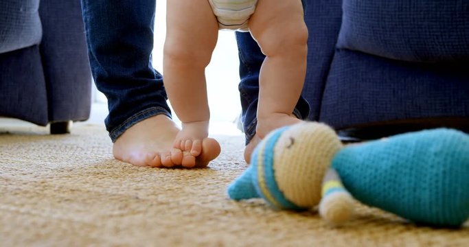 Father helping his baby boy to walk in living room 4k
