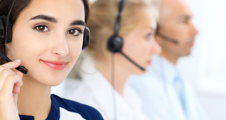 Call center operators at work. Focus at beautiful latin american woman in headset