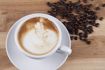 Hot cappuccino or latte art coffee. A cup of coffee on the wooden table with roasted beans. Morning breakfast with coffee. Flowers shape created by pouring steamed milk.