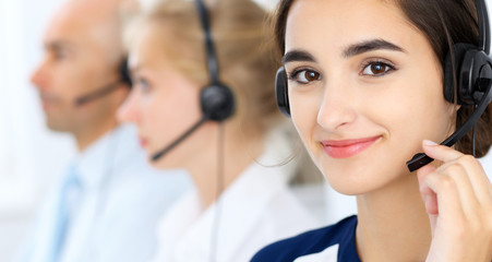 Call center operators at work. Focus at beautiful latin american woman in headset