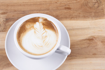 Hot cappuccino or latte art coffee. A cup of coffee on the wooden table with roasted beans. Morning breakfast with coffee. Hearts shape created by pouring steamed milk.