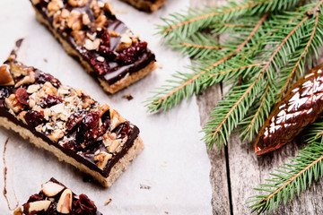 Obraz na płótnie Canvas Baked shortbread sticks with chocolate, chopped nuts and dried cranberries glazed. .Millionaire's shortbread cookies and fir branches on vintage wooden table. Christmas baking